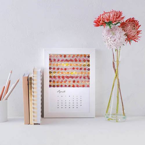 Calendar page for August is a watercolor geometric design in a white frame on a white desk