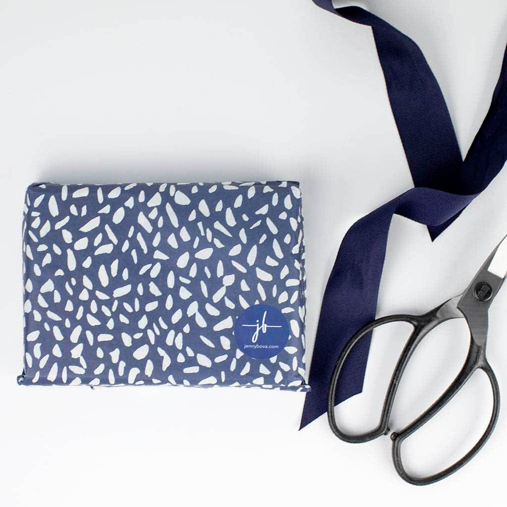 blue and white flecked tissue paper with jenny bova sticker, ribbon, and scissors on white