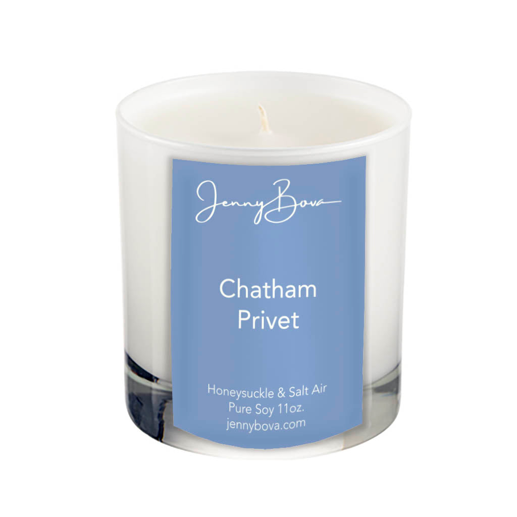 11 oz soy candle in a white glass jar with white wax. On the front of the jar is a periwinkle blue label with the Jenny Bova logo, the name of the candle, &quot;Chatham Privet&quot;, and product details. The background of the image is white.