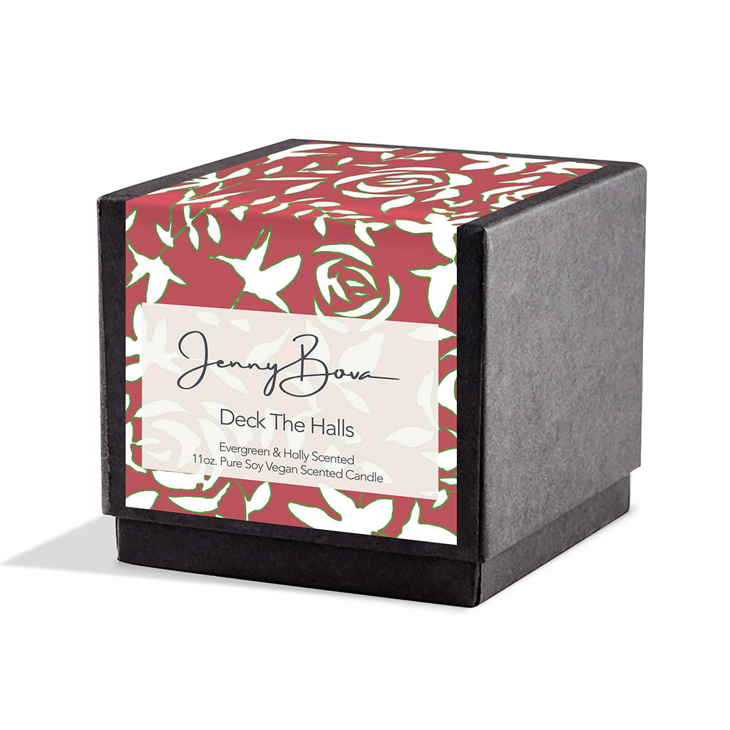 Square black candle box with a label covering front and top. The label is red with white flowers that are outlined in green. On the front are the Jenny Bova logo, the name of the candle, &quot;Deck The Halls,” and product details. The background is white.