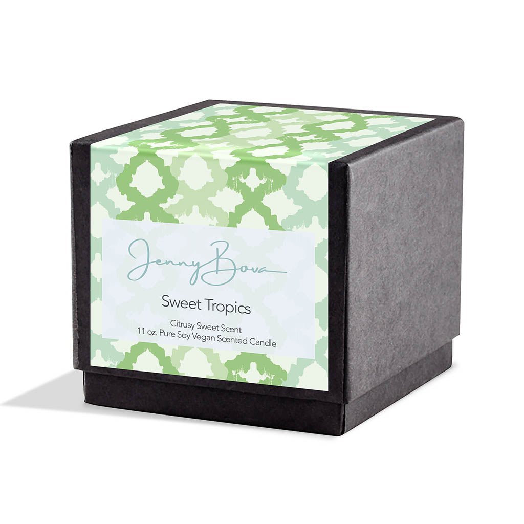 Square black candle box with a label covering the front and top. The label is a blue, green, and cream geometric design. On the front are the Jenny Bova logo, the name of the candle, &quot;Sweet Tropics,” and product details. The background is white. 