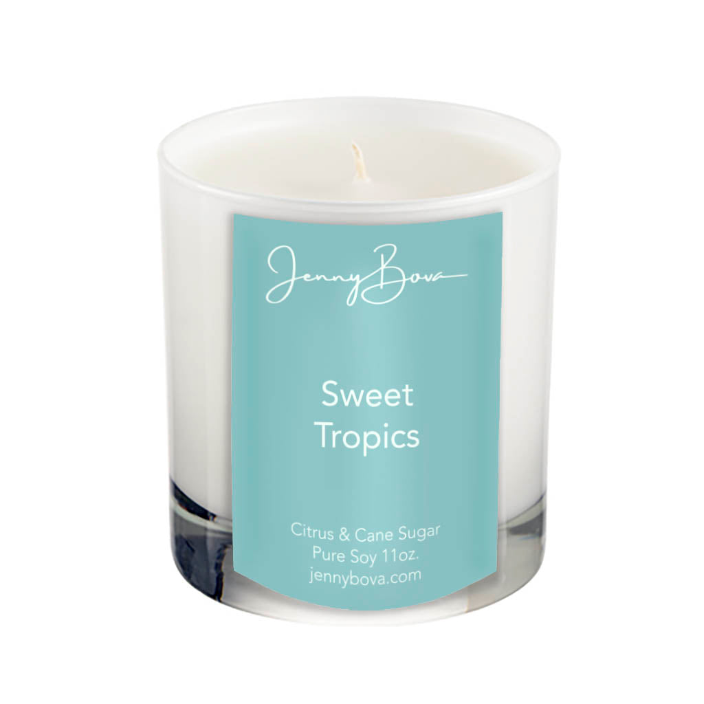 11 oz soy candle in a white glass jar with white wax. On the front of the jar is an aqua label with the Jenny Bova logo, the name of the candle, &quot;Sweet Troics&quot;, and product details. The background of the image is white.