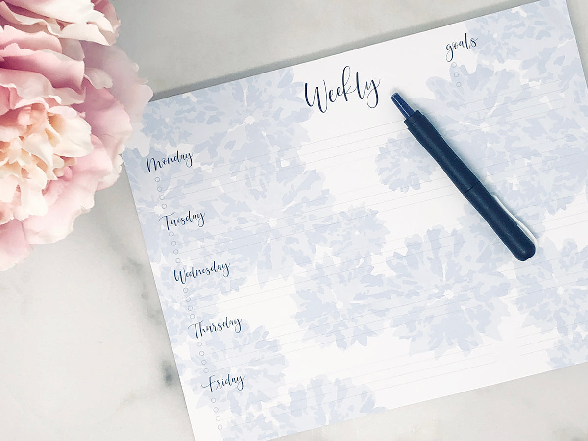 Weekly notepad blue on white with black type on desk