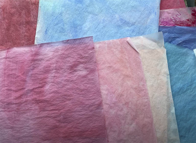 image of painted papers in pinks, reds, and blues overlapping on a flat surface