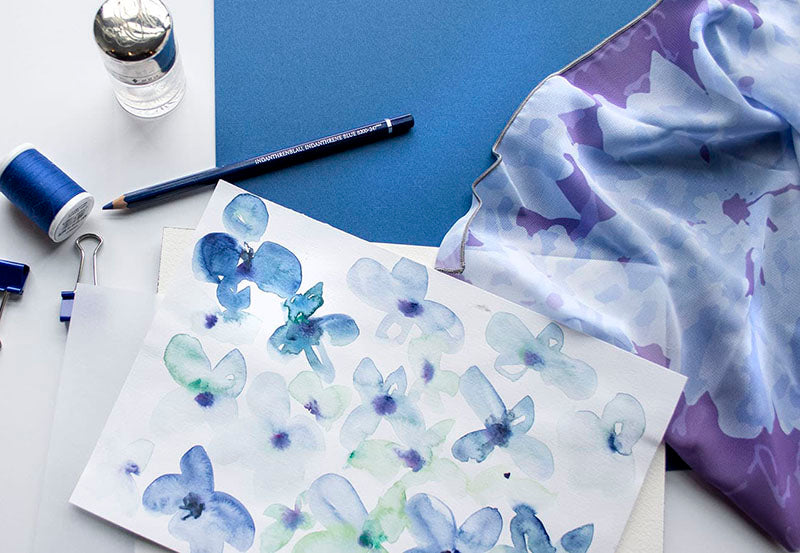 watercolor floral artwork with thread, fabric, and art supplies on a blue and white background