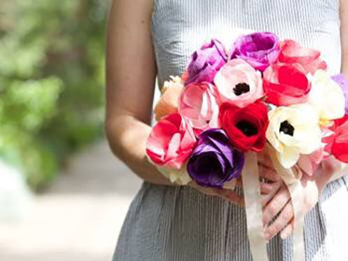 image of woman in a blue and white dress holding a bouquet of purple, pink, red, and white handmade paper flowers. 