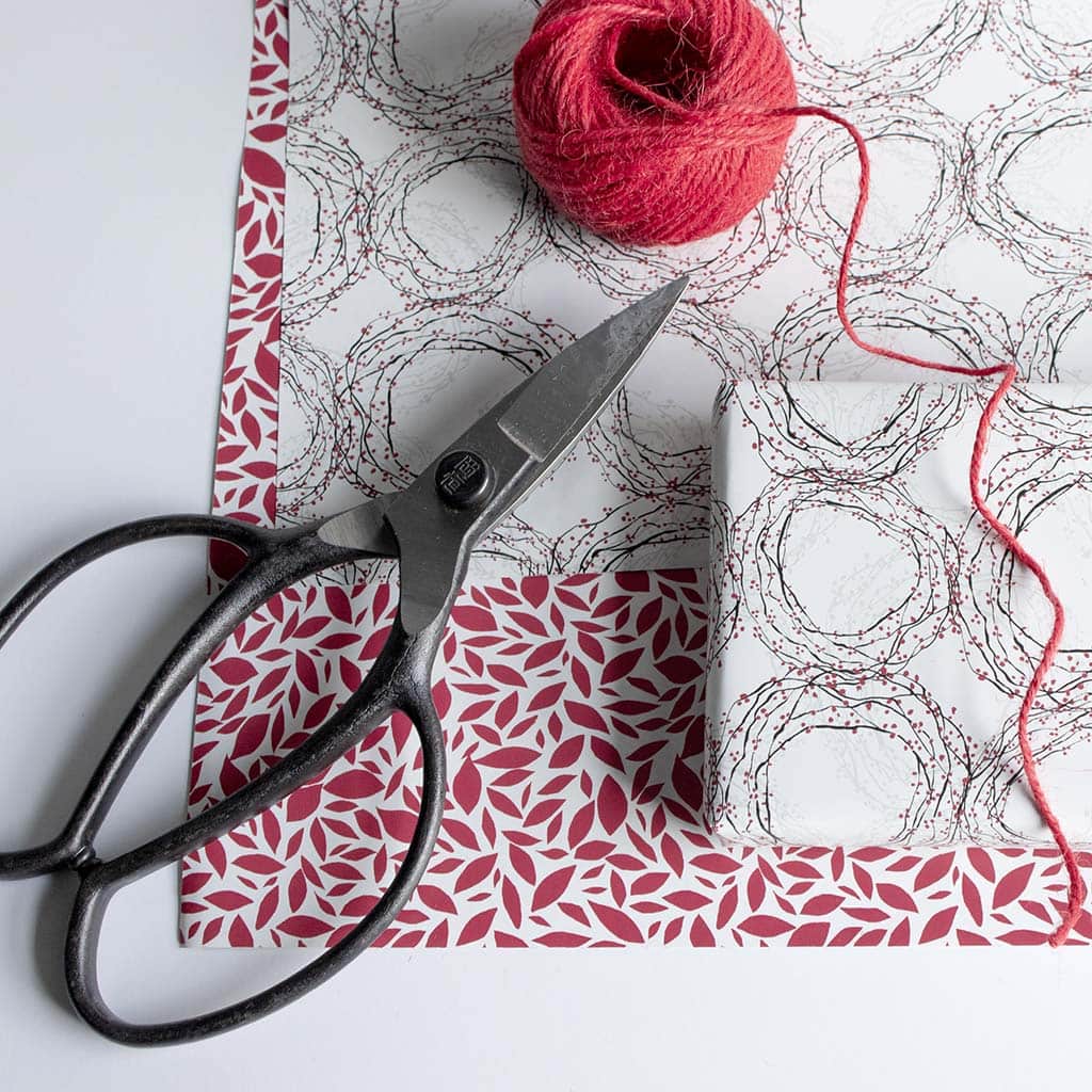Red and white patterned gift wrap under wreath patterned gift wrap with scissors and red twine