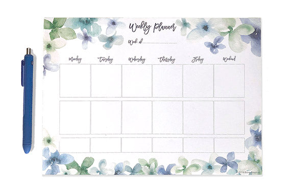 jenny bova's weekly planner page download freebie sitting on a white surface with a blue pen next to it. The planner page has blue and green watercolor flowers around the edges and slots for each day of the week. 