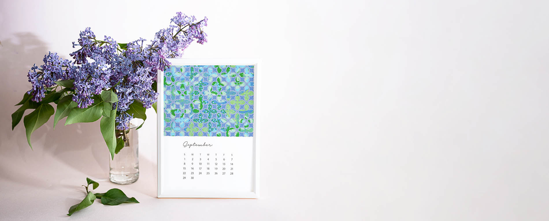 A framed 2024 Calendar page of the month of September. The page features Jenny Bova's artwork. The background is white. To the left of the frame is a vase of blue flowers. 
