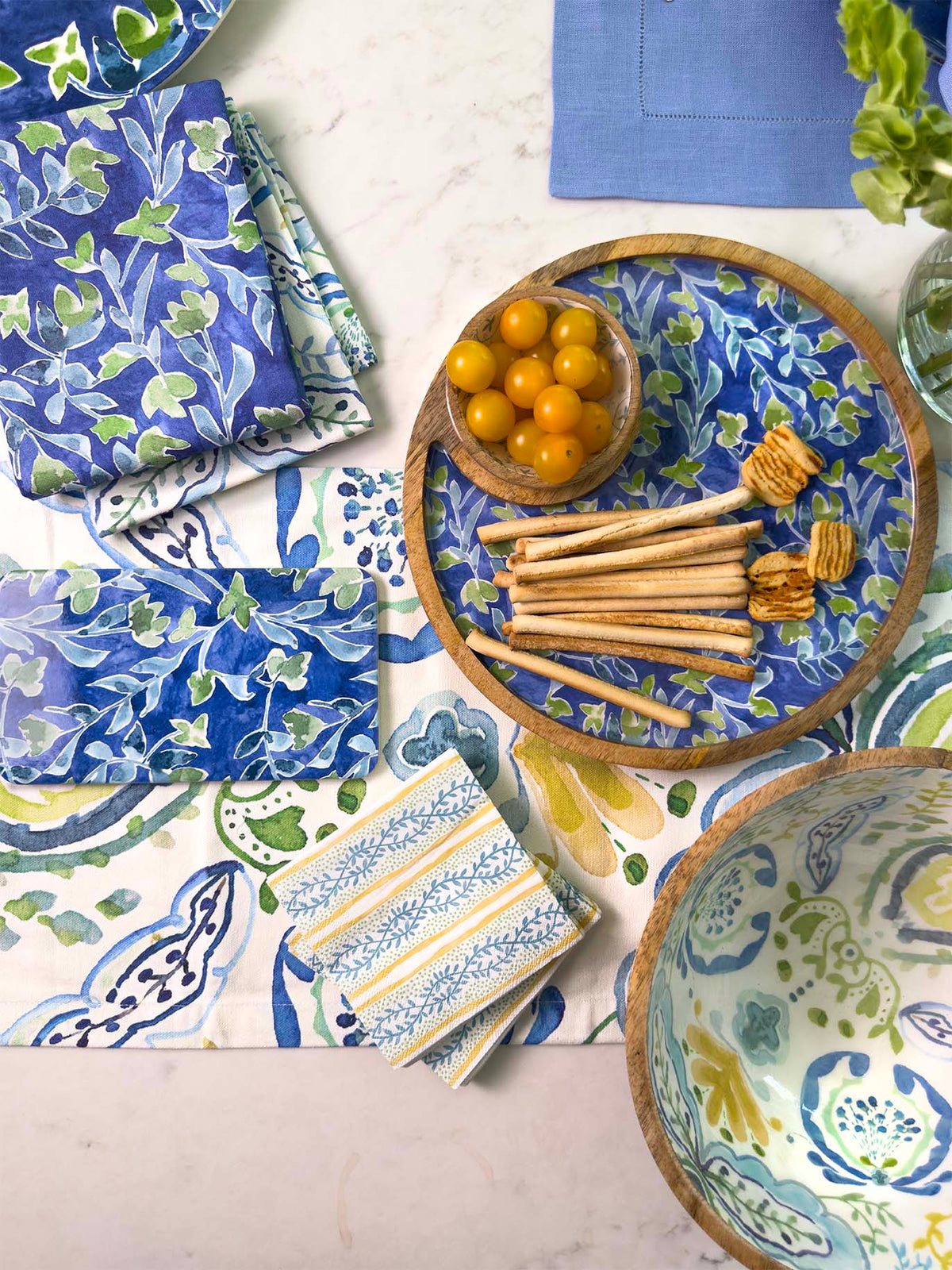 Table setting with blue and green watercolor patterned tableware, including bowls and napkins.