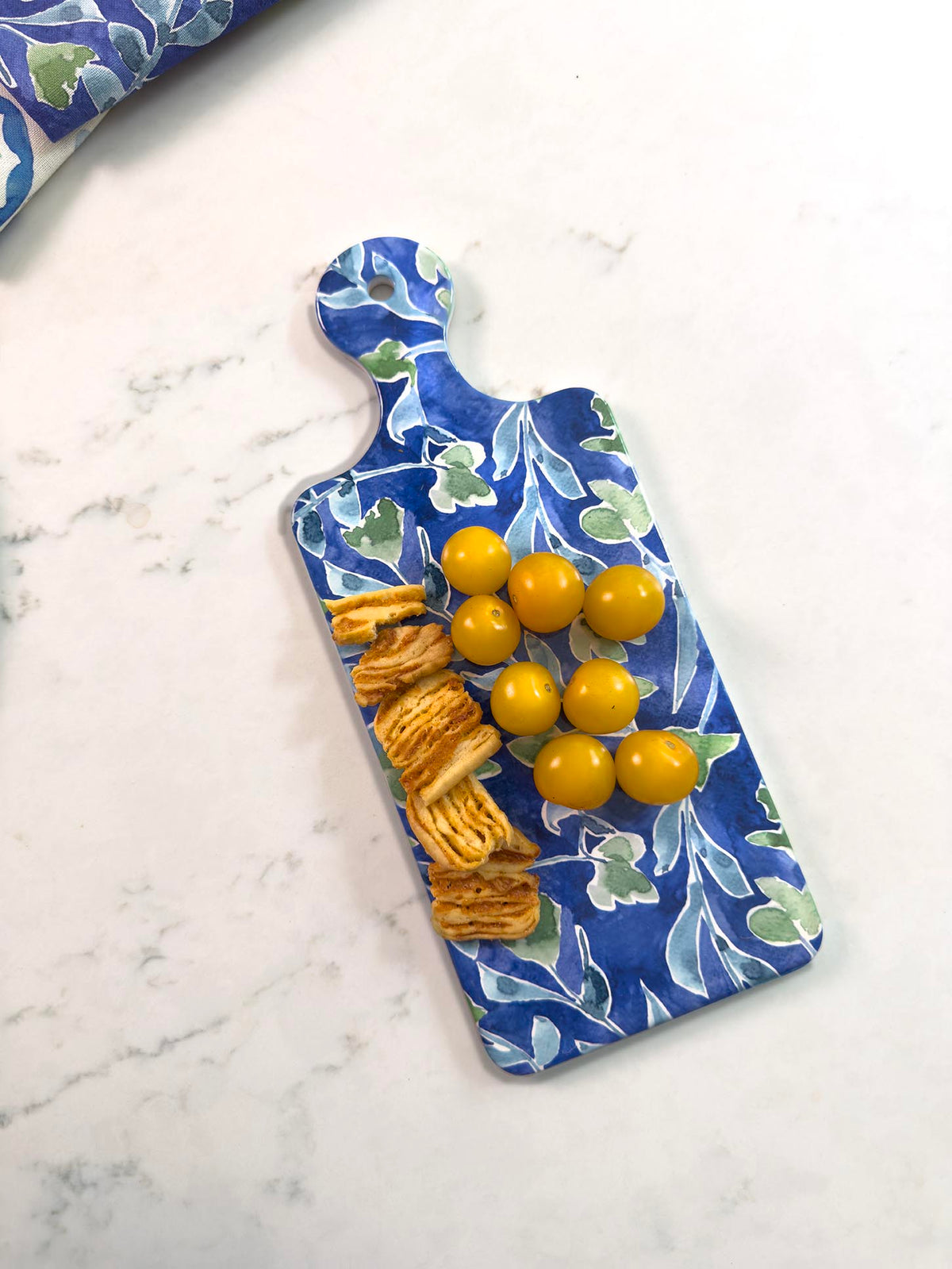 Blue decorative cutting board with yellow tomatoes and crackers on a marble surface