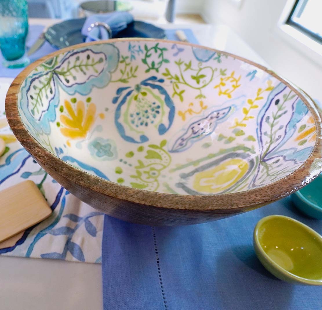 Decorative mango wood bowl with floral patterns on a blue tablecloth