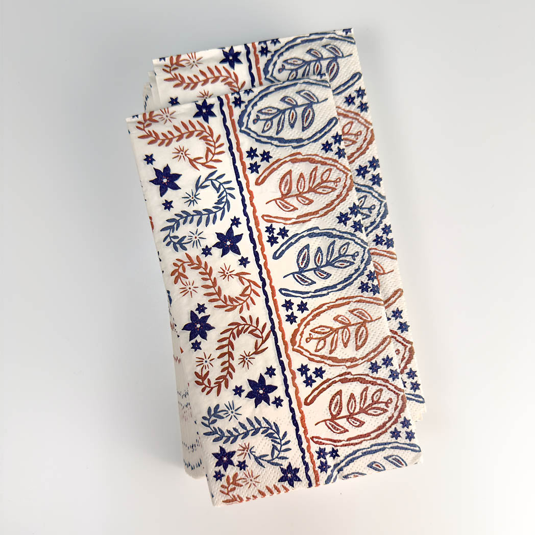 A tall, narrow paper gift bag with a cream-colored background and a hand-block printed pattern in navy blue and terracotta red. The pattern features stylized leaves, stars, and floral motifs.