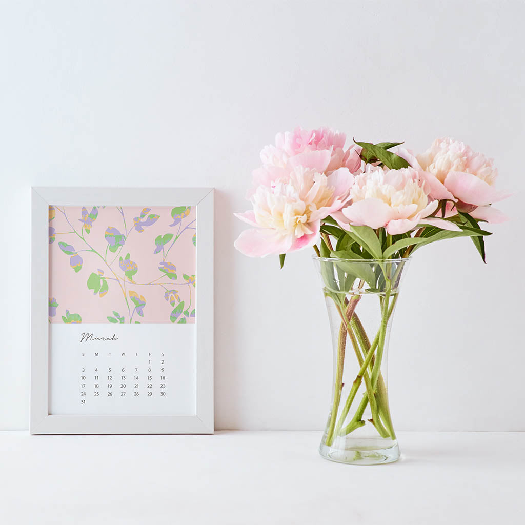 A 5x7 card with the days and dates for March 2024 and a pink floral illustration in a white frame. Next to the fram is a bouquet of pink peonies. 