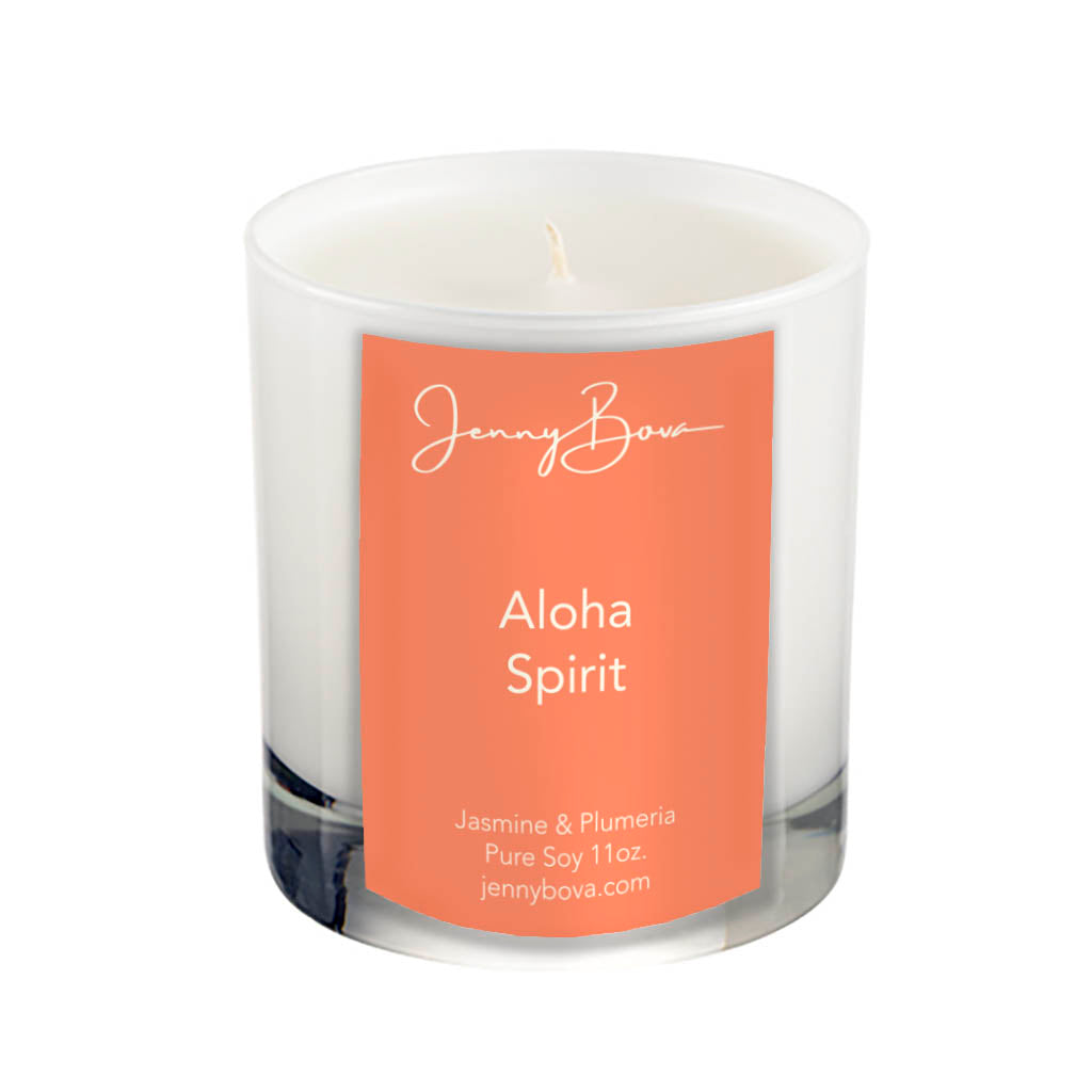 11 oz soy candle in a white glass jar with white wax. On the front of the jar is an orange label with the Jenny Bova logo, the name of the candle, &quot;Aloha Spirit&quot;, and product details. The background of the image is white.