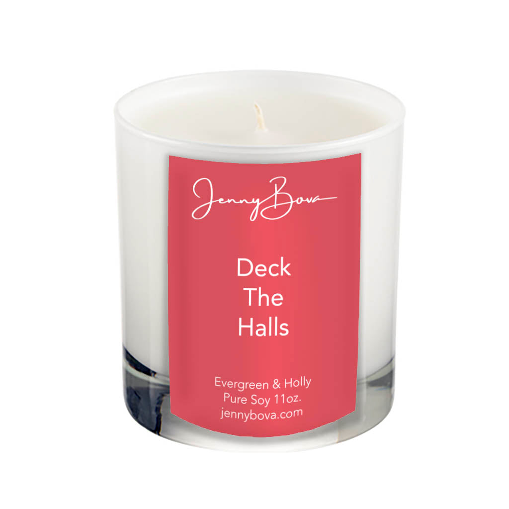 11 oz soy candle in a white glass jar with white wax. On the front of the jar is a red label with the Jenny Bova logo, the name of the candle, &quot;Deck The Halls&quot;, and product details. The background of the image is white.