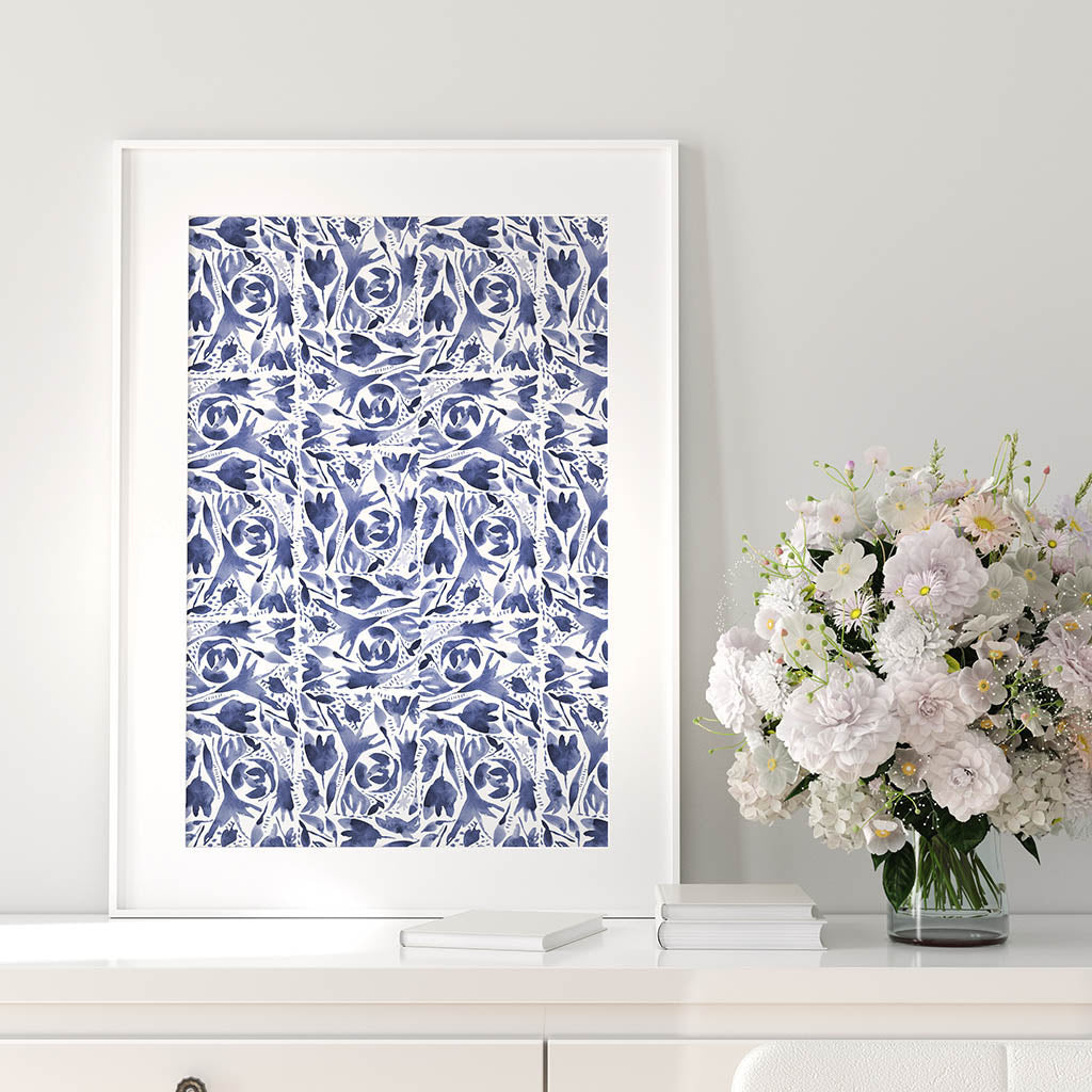 Indigo watercolor folk design art print shown at 16x20 inches in a white frame leaning up against a gray wall. White and pink flowers on white sideboard next to frame
