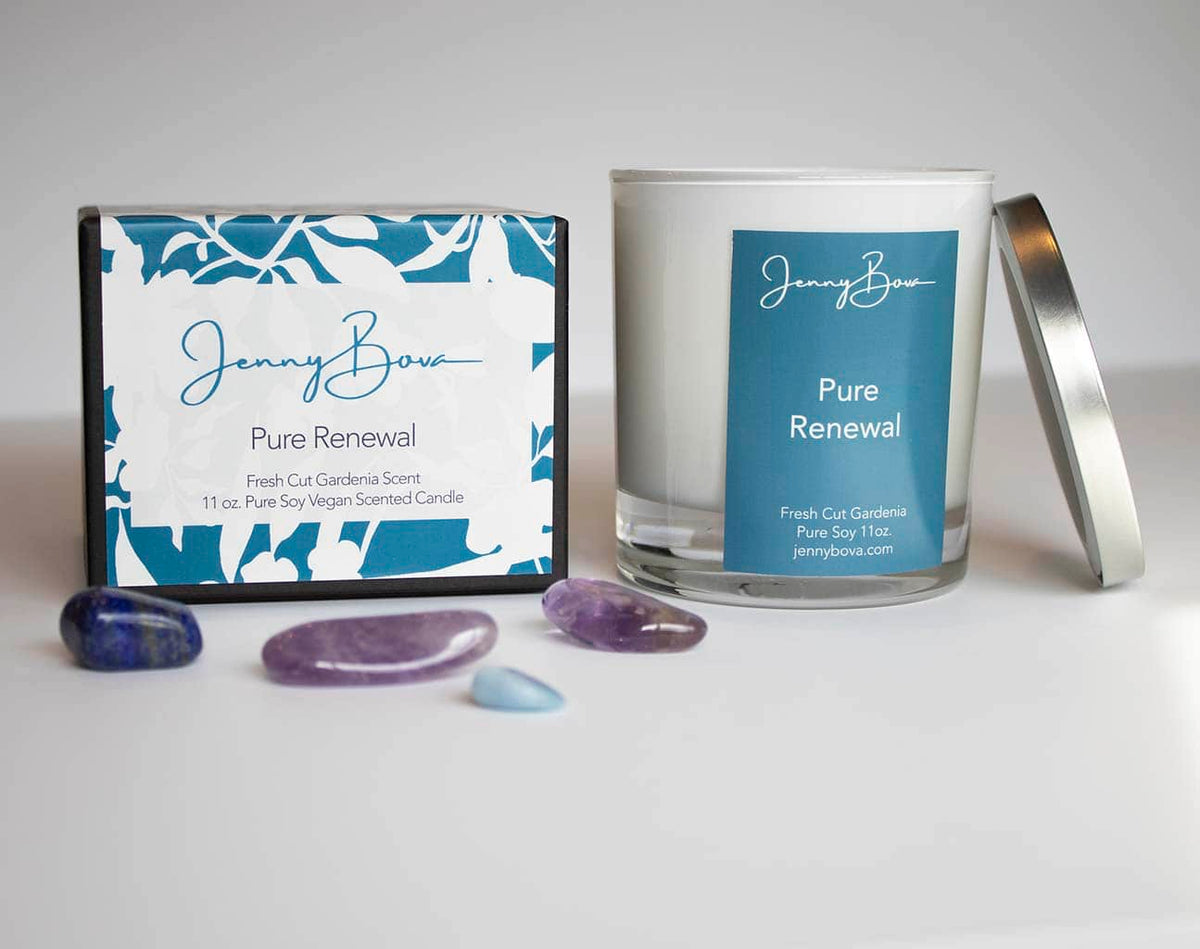 Gardenia scented soy candle with a blue label and cover leaning against the candle. Next to it is a black candle box with a blue floral patterned label. In front of the box are blue and purple crystals. 