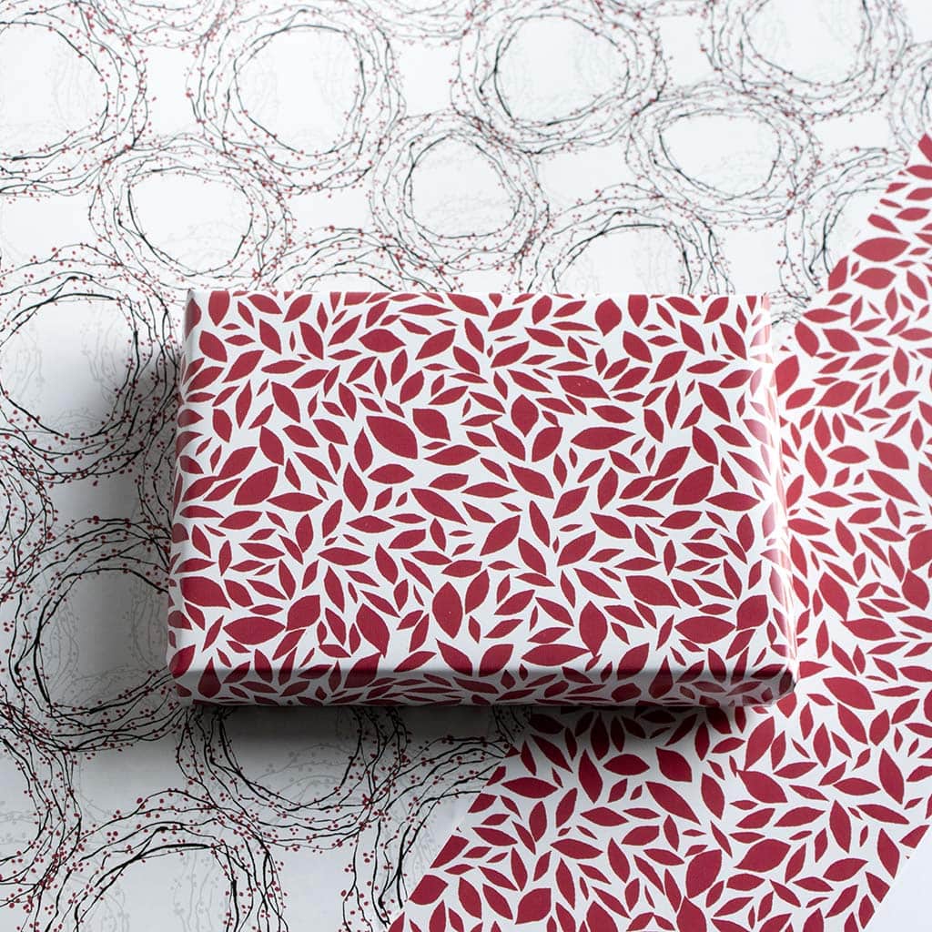 Red and white gift wrap for holidays or other occasions. Small abstract red pattern on a white background. Below the package is paper with the wreath pattern