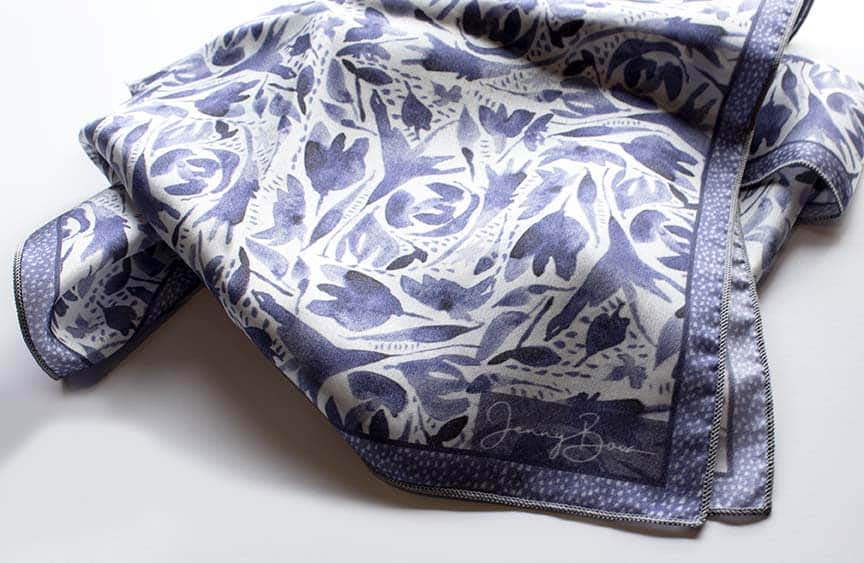 corner detail of a silk scarf with a blue and white watercolor design. The Jenny Bova logo is printed on the corner shown.